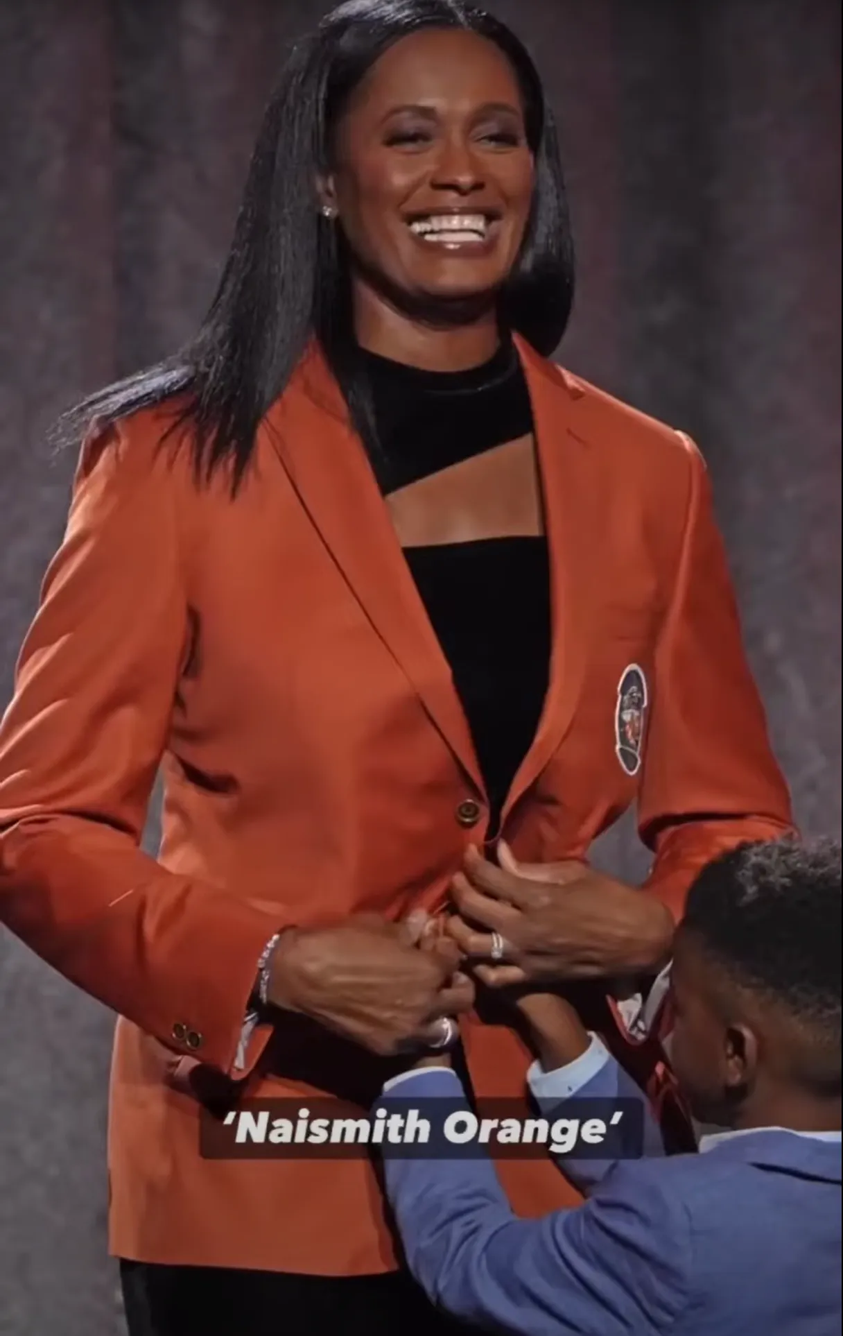 Woman smiling and wearing Reveal Blazer with the caption: Naismith Orange